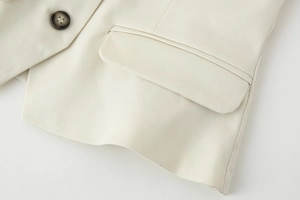 Close-up of beige vest featuring a flap pocket with dark button and woven fabric texture