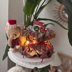 Christmas teddy bear with red hat and scarf beside a gift box with warm LED lights