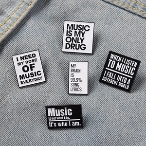 Five music theme metal badges pinned on denim fabric with black and white quotes