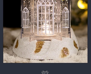 Close-up of a glowing Christmas crystal church house music box with warm LED lights and snow