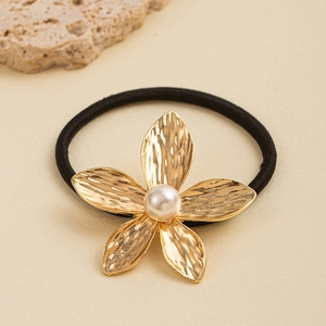 Detailed close-up of a golden textured flower hair tie with a white pearl center