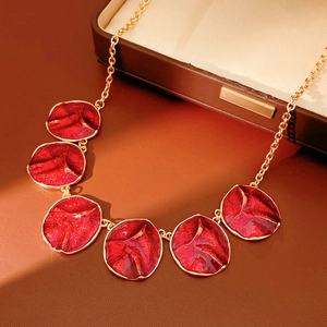 Detail of gold necklace with red enamel textured pendants on a leather surface