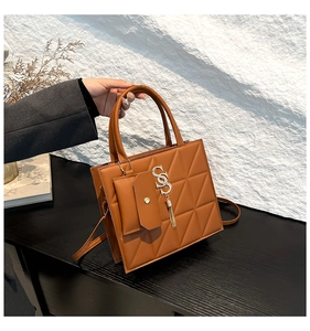 Detail of brown geometric quilted handbag with gold SS letter metal charm and tassel