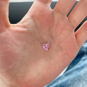 Handheld view of a heart-shaped pink zircon pendant on a delicate silver chain