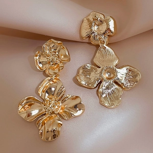 Détail macro de boucles d'oreilles fleur dorées sur fond de soie beige élégant