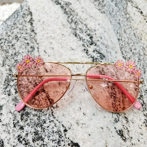 Close-up of golden frames with pink lenses and small enamel daisy flower decorations