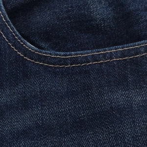 Gros plan détaillé des doubles coutures sur les poches en jean bleu foncé de la veste