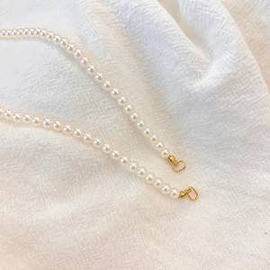 Detailed macro view of white faux pearls on a simple stainless steel necklace with gold clasp