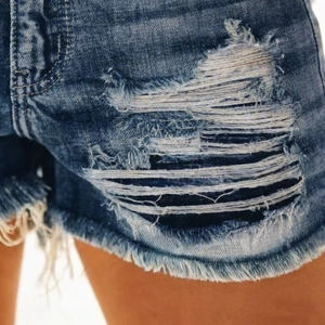 Detail of ripped blue denim shorts with distressed frayed edges and washed texture