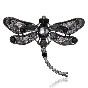 Detailed view of dragonfly brooch with grey crystals on a dark alloy base with reflection