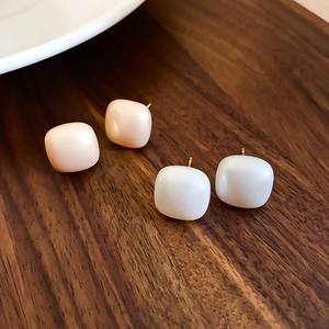 Detail of square resin stud earrings in white and pink with gold plated silver needles