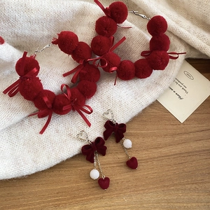 Detail of red pompom and velvet bow earrings with pearls on white knit fabric