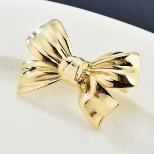 Minimalist gold bow brooch with a high-polished metallic finish on a white background
