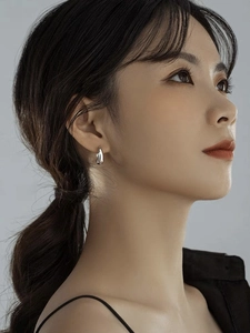 Close-up of minimalist silver water drop earrings on model with metallic luster
