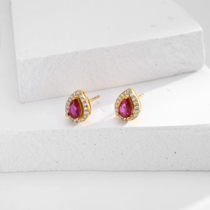Macro shot of gold pear-cut red gemstone stud earrings with white zircon halo on white stone