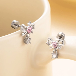 Silver bow earrings with pink heart and clear round gems on a beige ceramic cup