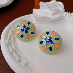 Detail of enamel flower earrings with blue petals and pink hearts on light green base