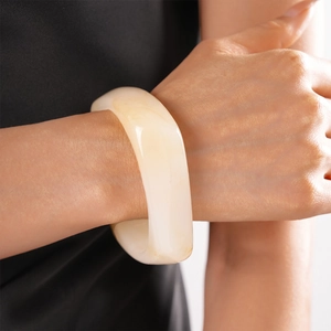 Close-up of a wide chunky resin bangle in cream white on a female wrist for vintage look
