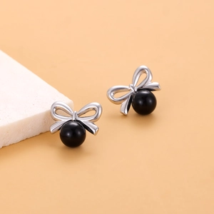 Vue macro détaillée de boucles d'oreilles nœud avec perle noire sur plateau blanc