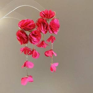 Detail of fuchsia fabric flower tassel earrings with golden chains on neutral background