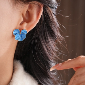 Gros plan de boucles d'oreilles pensée en émail bleu avec bord doré sur modèle