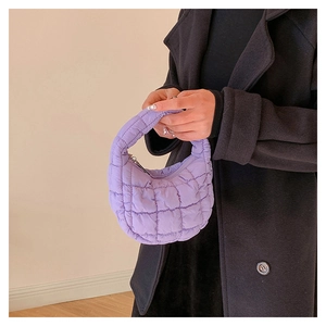 Close-up of a purple quilted puff mini tote bag held by a model in a black coat