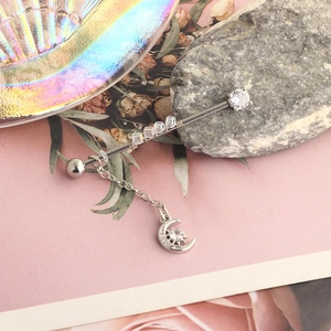 Close-up of silver industrial barbell with crescent moon charm and crystal accents