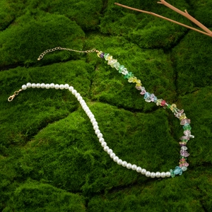 Fashion necklace with half white pearls and colorful stones on green moss background