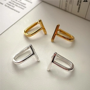 Detail view of gold and silver T-shaped minimalist earrings on white leather texture