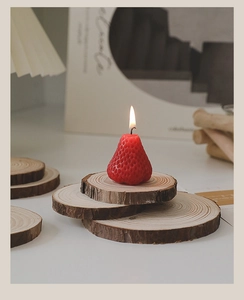 Detail of a burning red strawberry shaped scented candle on a layered wooden base