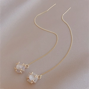 Detail of long gold earrings with faux cat eye stone on champagne satin fabric