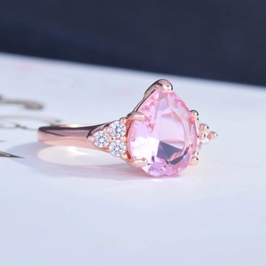 Rose gold pear cut pink diamond ring with white accent stones on a sleek band