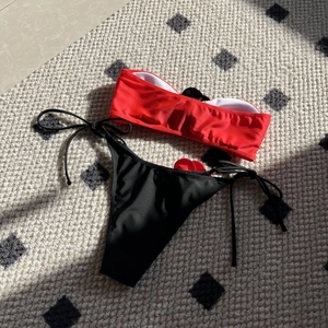 Detailed flat lay of red bandeau bikini top and black side-tie bottoms on textured mat
