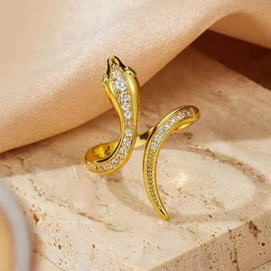 Macro shot of a golden snake-shaped ring with zircon stones on a beige stone surface