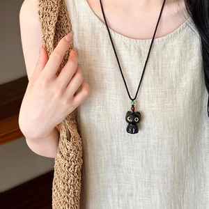 Collier pendentif chat noir créatif avec cordon tressé porté sur une robe en lin
