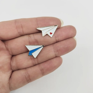 Minimalist paper plane enamel brooches with heart and blue tail held in hand