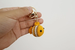 Hand holding a crochet clownfish keychain in golden yellow with white and brown stripes