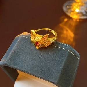Macro detail of 24k gold plated fox ring with red and green gemstone accents on velvet