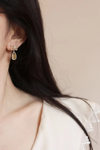 Detail of silver needle zircon bowknot earrings featuring a yellow teardrop gemstone