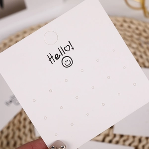 Macro detail of white cardboard earring display card with multi-hole slots and smiley logo