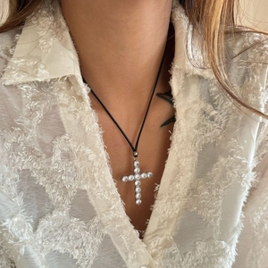 Detail of silver cross pendant with clear zircons and black cord on a white shirt