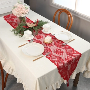 Festive red lace Christmas table runner with tassels over white ruffled tablecloth
