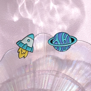Space theme enamel pins featuring a rocket and planet on a decorative shell tray