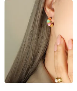 Detail of vintage enamel C-shaped earrings and a gold pearl ring on a model