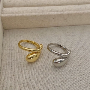 Close-up of dual-layer liquid teardrop rings in gold and silver on a beige fabric base