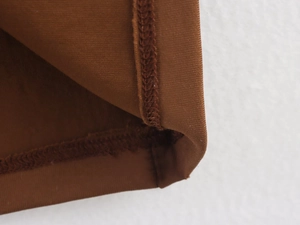 Detailed close-up of brown dress hem showing precise stitching and fine fabric texture