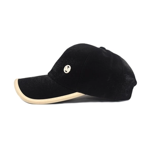 Detail of black satin baseball cap featuring a white M logo emblem and beige edge piping