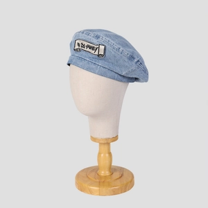 Close-up of denim beret featuring an embroidered patch with artistic lettering detail