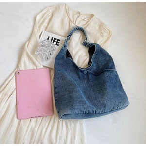 Detailed flat lay of blue denim tote bag with round hardware on white dress backdrop