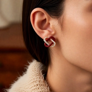 Macro side view of interlocked red enamel and gold-plated zircon earrings on a model